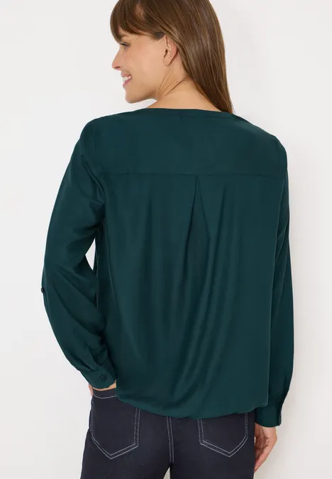 Frau mit langen Haaren trägt grüne Bluse und Jeans, Blick von hinten.